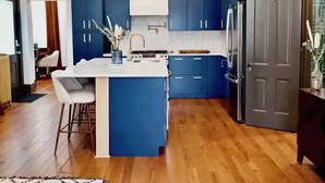A modern kitchen with blue cabinets, a central island, and a stainless steel refrigerator.