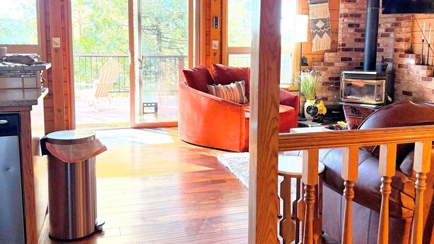 Een ruim interieur van een blokhut met een groot houten plafond, een stenen openhaard en een gezellige zithoek met een rode bank en een houten tafel.