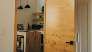 Une pièce avec une porte en bois, un lit et un coin cuisine visible à travers une porte ouverte.