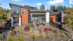 A modern two-story house with large windows, a patio with outdoor seating, and a landscaped garden with various plants.