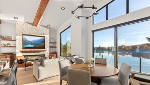 A modern living room with a stone fireplace, a flat-screen TV, and a dining area with a view of a lake.
