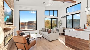 A spacious living area with a fireplace, a sofa set, a dining table, and large windows offering scenic views.