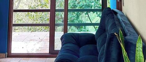 Ein Zimmer mit einer großen Schiebeglasdoor, die auf eine Terrasse führt. Auf der rechten Seite befindet sich ein dunkelblaues Sofa und ein Blumentopf. An der Wand ist der Schriftzug 'Rancho Paraíso Real' zu sehen.