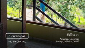 A view from a window with a metal staircase leading outside, surrounded by greenery. Text on the image includes a logo, a contact number, and a location in Mexico. - Rancho Real Paraiso (Amealco)