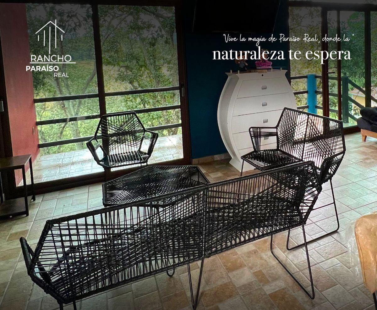 Interior moderno com mobiliário de metal preto, grandes janelas com vista para vegetação, e informações de contato para Rancho Paraíso Real.
