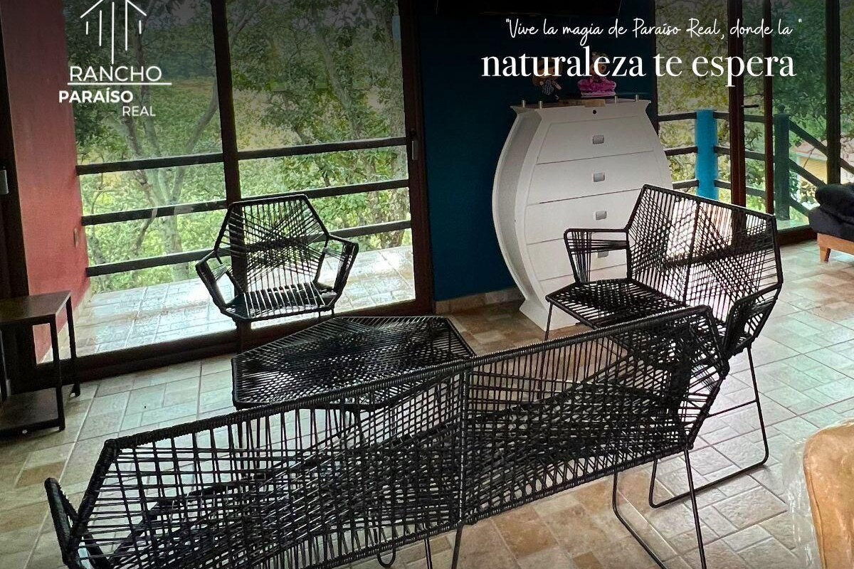 Ein modernes Interieur mit schwarzer Metallmöbeln, großen Fenstern mit Blick auf Grünflächen und Kontaktinformationen für Rancho Paraíso Real.
