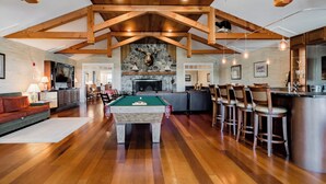 A spacious living area with a pool table, wooden ceiling beams, a stone fireplace, and a bar area with stools. - Resort style, family friendly getaway! (Lincolnville)