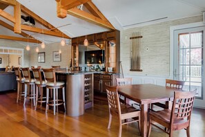 A spacious kitchen with wooden beams, a central island with bar stools, and a dining area with a large table and chairs. - Resort style, family friendly getaway! (Lincolnville)