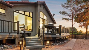 A modern house with a large deck, a staircase leading to the entrance, and a well-lit driveway. - Luxury Desert Retreat w/ Hot tub + Fire Pit! (Sedona)