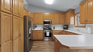 Una cocina con armarios de madera, electrodomésticos de acero inoxidable y encimera blanca.