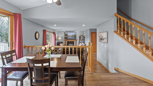 Un comedor con una mesa y sillas de madera, un ventilador de techo y una escalera con barandillas de madera.