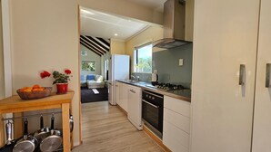 A modern kitchen with white cabinets, a stove, and a dining area with a table and chairs. - Charming Beach House (Ruby Bay)