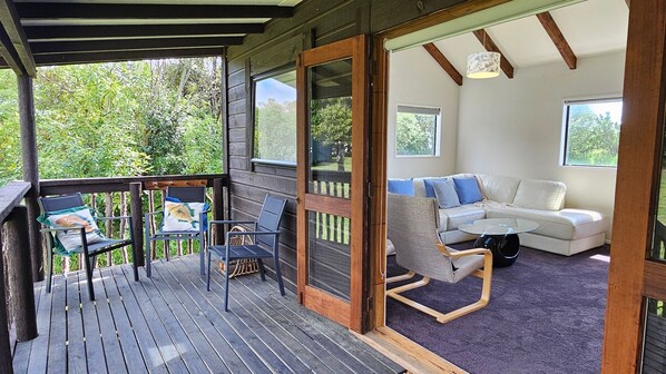 A wooden deck with outdoor seating, a sliding glass door leading to a living area with a sofa and a coffee table.