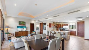A spacious living area with a large dining table, comfortable seating, and a kitchen in the background. - Treetop Ocean View Penthouse - Jobo 15 (Brasilito)