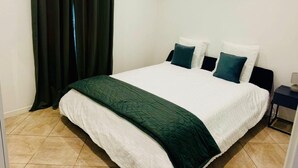 Uma cama bem arrumada com edredom branco e verde, duas almofadas e um manta verde escura.