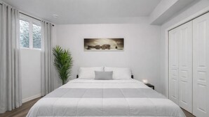 Un dormitorio moderno con una cama grande, cortinas blancas, una planta en maceta, una mesita de noche y un cuadro en la pared.
