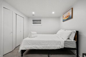 Une chambre à coucher avec un lit, des rideaux blancs, une fenêtre avec des stores et un tableau au mur.