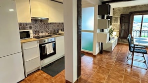 A modern kitchen with white cabinets, a stove, and a microwave. There is a dining area with a table and chairs, and a view of the city through a large window. - Charming apartment in the best area of downtown Vigo (Vigo)