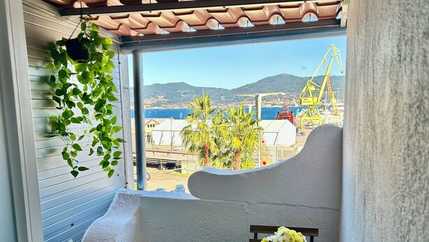A balcony with a view of the sea and mountains, a wooden bench, a small table with a vase of flowers, and hanging plants. - Charming apartment in the best area of downtown Vigo (Vigo)