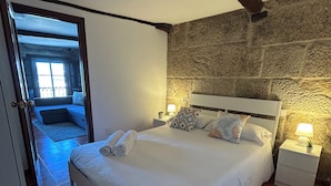 A bedroom with a large bed, a stone wall, a wooden ceiling beam, and a nightstand with a lamp. - Charming apartment in the best area of downtown Vigo (Vigo)
