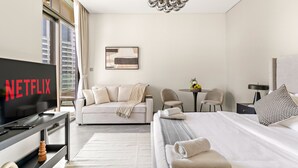 Een moderne hotelkamer met een groot bed, een bank, een televisie waarop 'NETFLIX' wordt getoond, een kroonluchter en uitzicht over de stad.