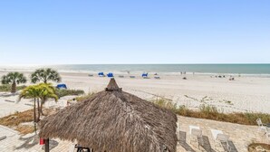 Une plage avec un abri à toit de chaume, des chaises longues et des palmiers.