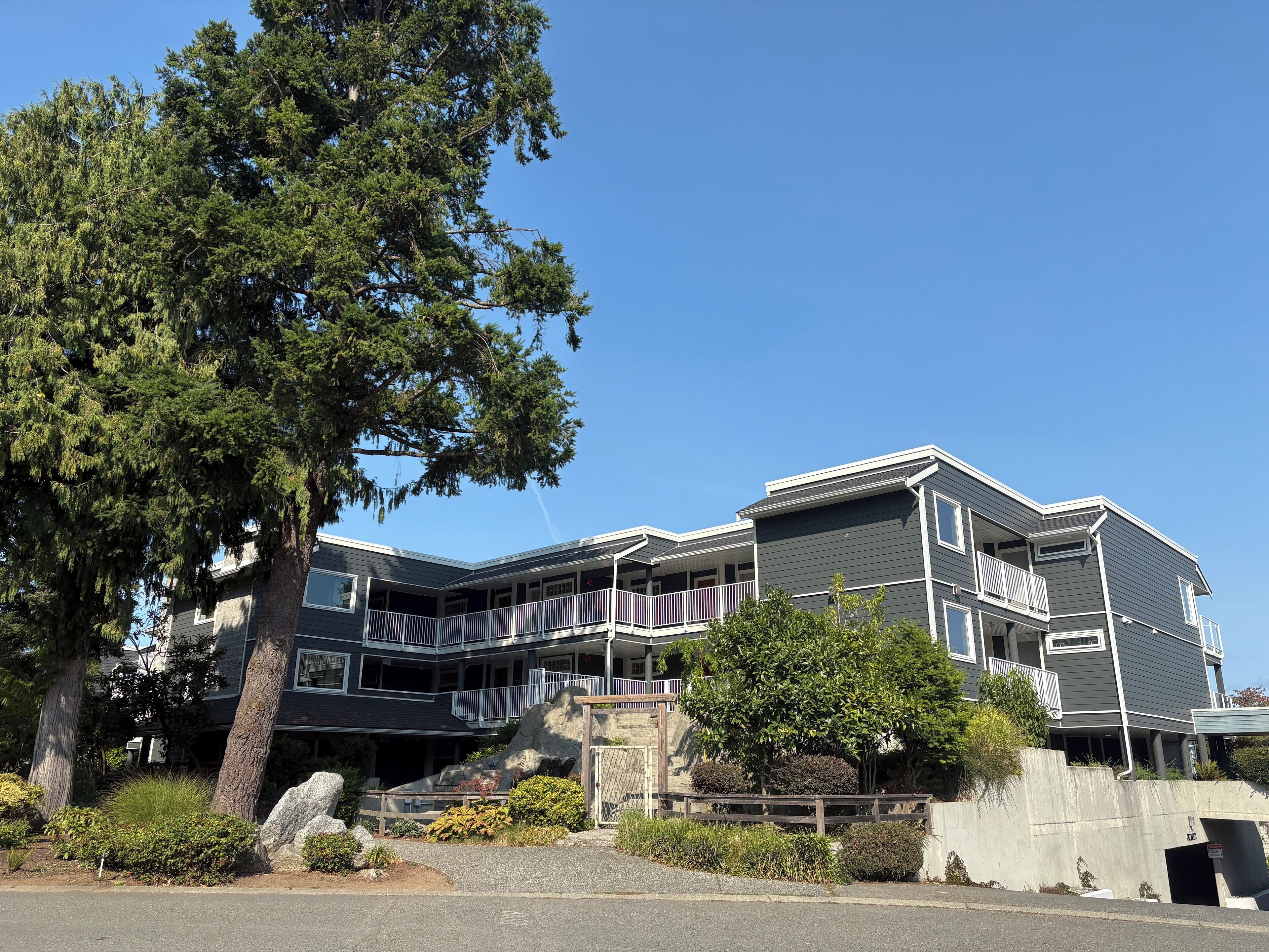 A multi-story building with balconies, a stone staircase, and a large tree in the foreground.