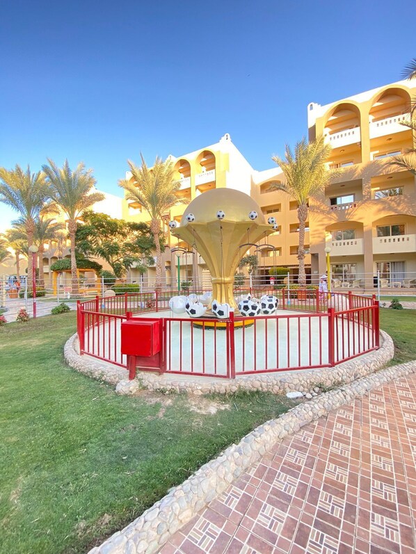 A courtyard with a fountain, palm trees, and a building with multiple balconies. - Nubia Aqua Beach Resort (Hurghada)