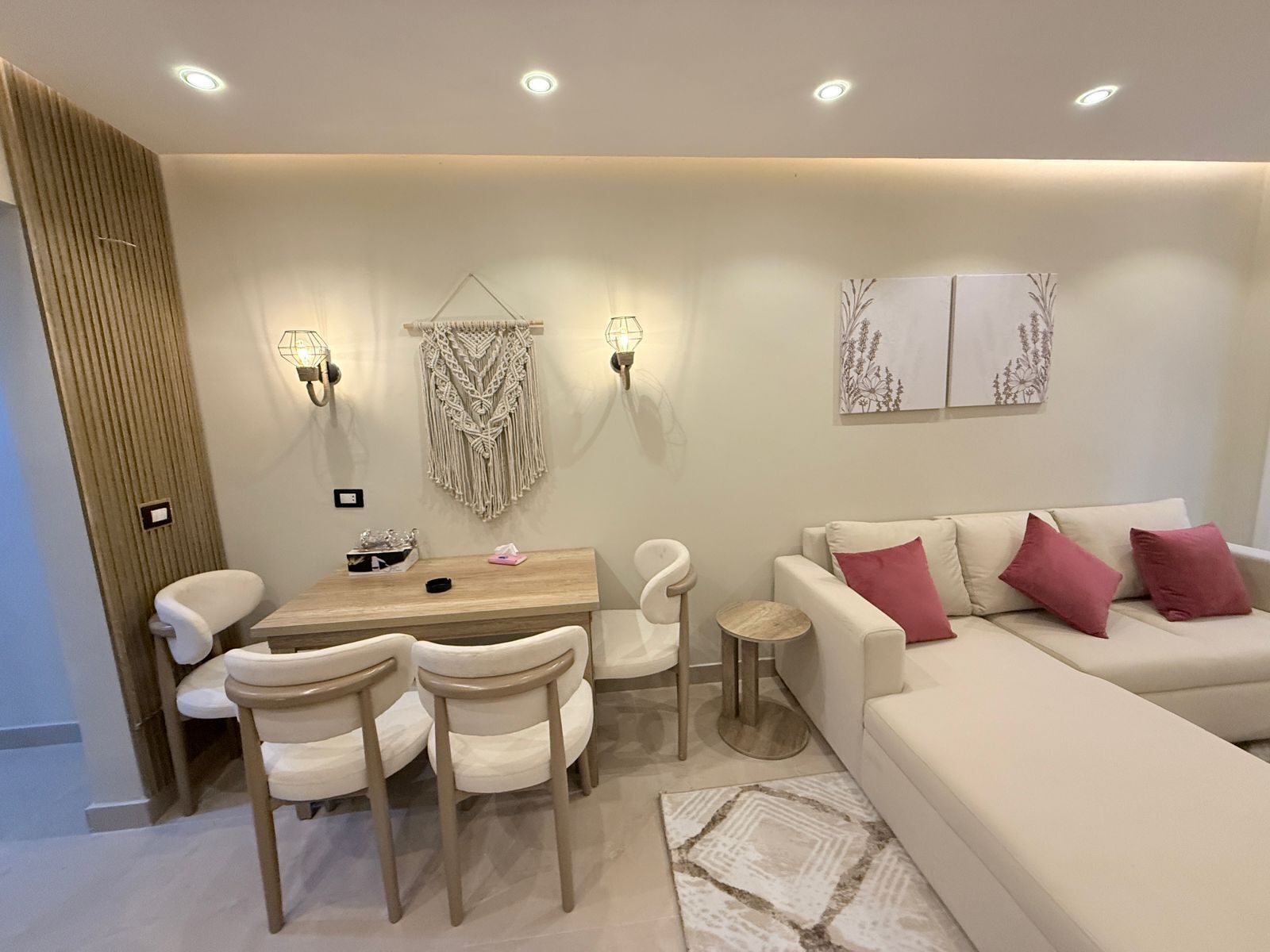 Un salon moderne avec un canapé beige, une table à manger en bois et des chaises, ainsi que des appliques murales.