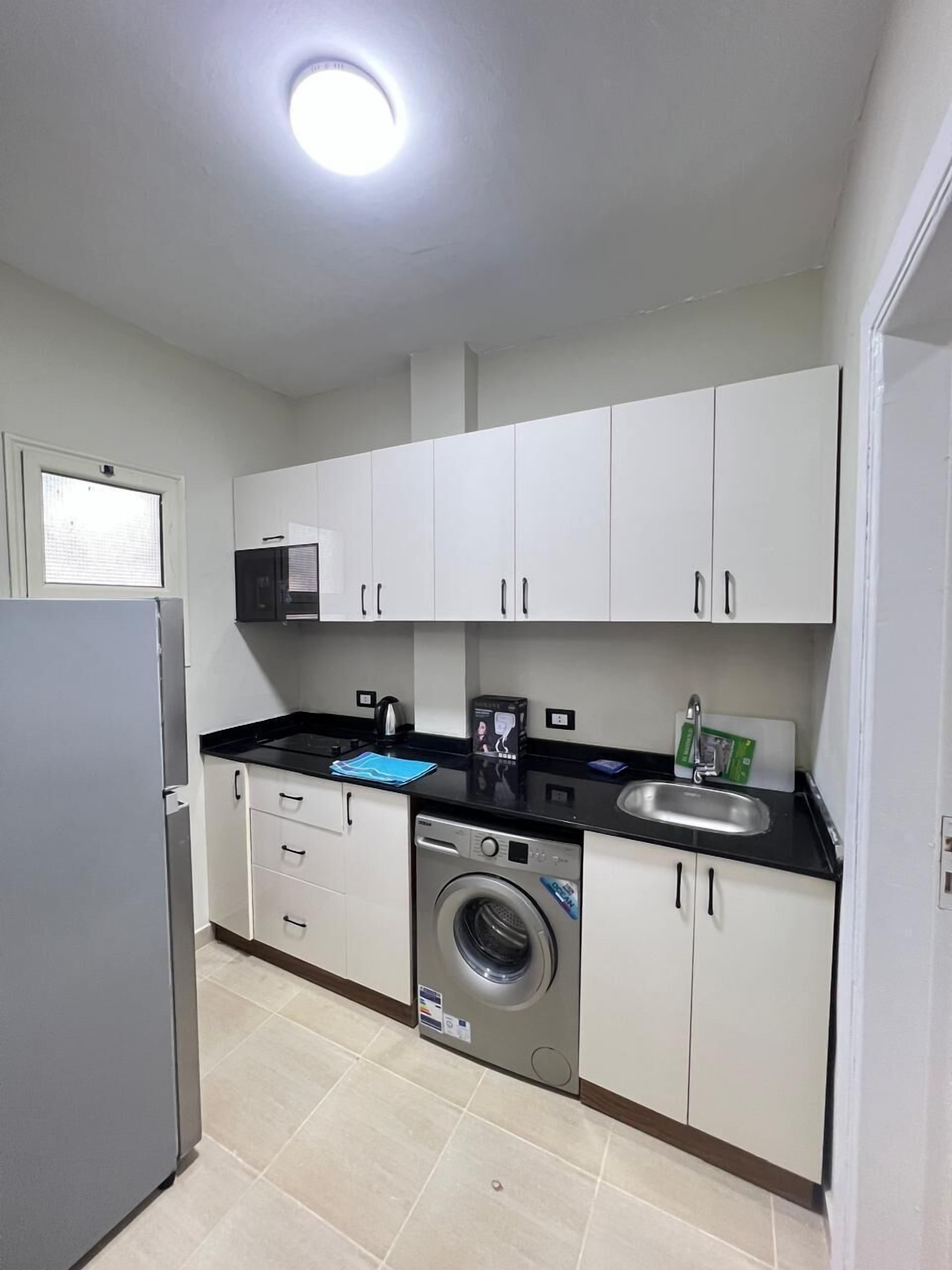 Una cocina compacta con armarios blancos, lavadora, microondas y refrigerador.