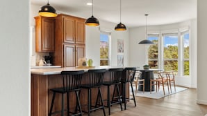 A modern kitchen with wooden cabinets, black bar stools, and pendant lighting.