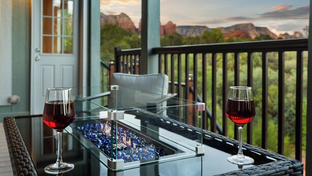 A glass table with two wine glasses on a balcony overlooking a mountainous landscape.