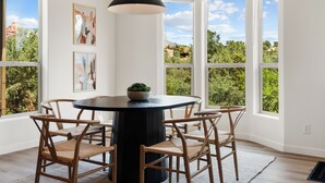 A dining area with a round table, four wicker chairs, a black pendant light, and artwork on the walls.