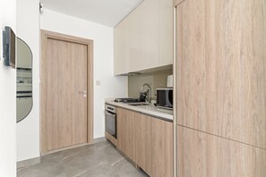 A modern kitchen with wooden cabinets, a microwave, and a stove. - Peninsula One - 2410 Studio (Dubai)