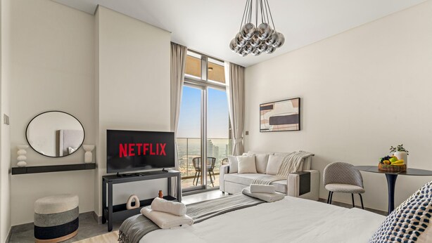 Une chambre d’hôtel moderne avec un grand lit, un téléviseur diffusant « NETFLIX », un balcon avec vue et une petite table avec des fruits.