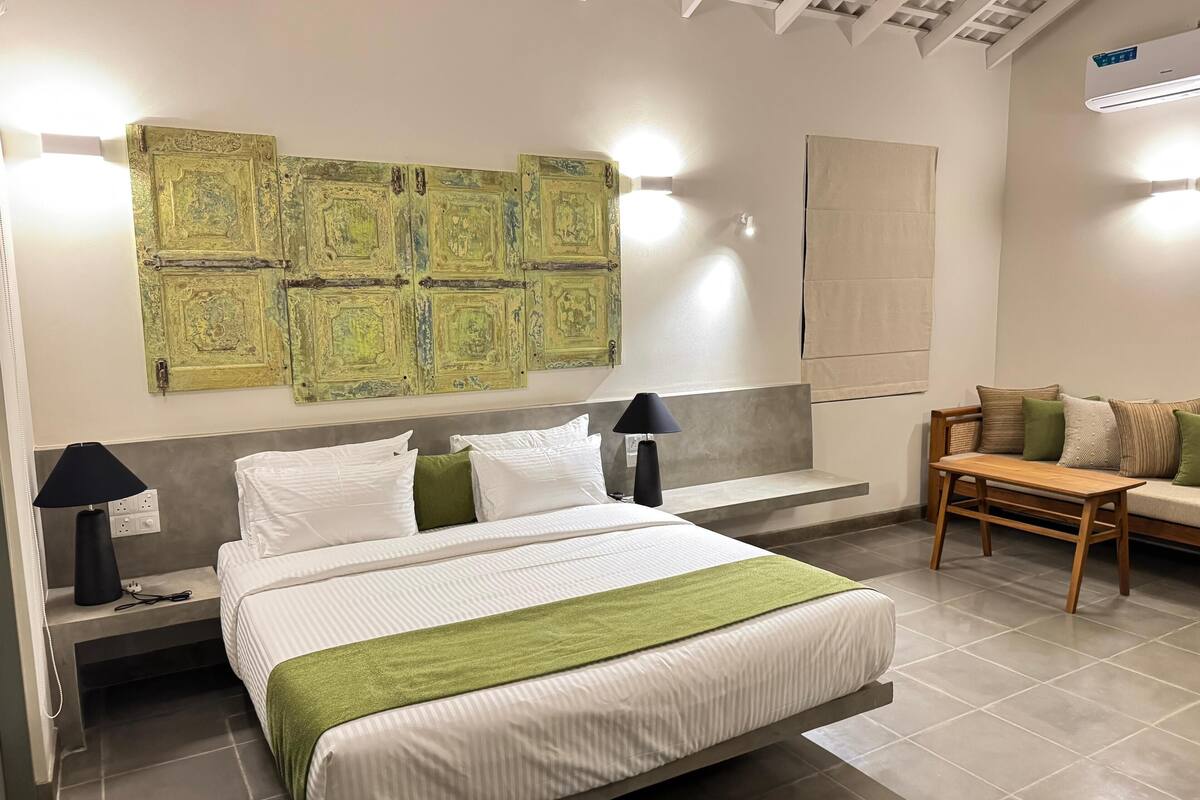 A modern hotel room with a large bed, bedside lamps, a wooden bench, and a wall-mounted air conditioner.