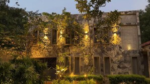 Un bâtiment en pierre doté de nombreuses fenêtres et d’un mur décoratif, entouré d’une végétation luxuriante et de plantes bien entretenues.