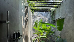Un petit espace douche avec un mur en pierre, une plante en bambou suspendue et une plante en pot.