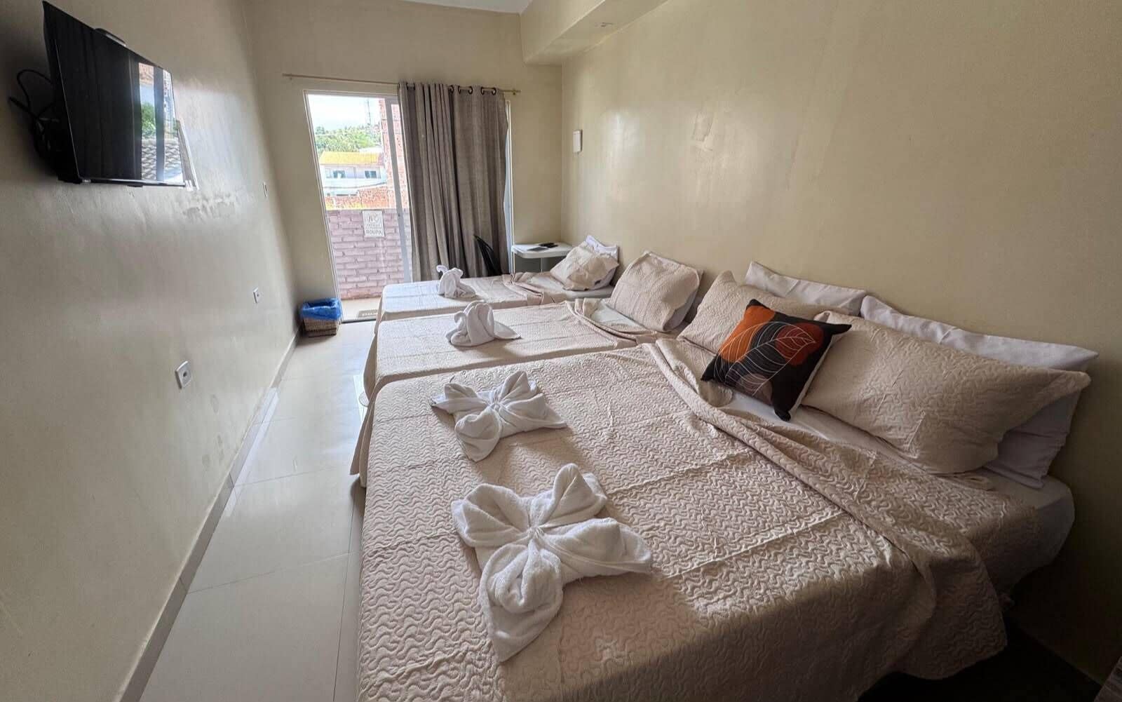 Habitación de hotel con dos camas, un televisor montado en la pared y vistas al exterior a través de una ventana.