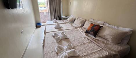 Habitación de hotel con dos camas, un televisor montado en la pared y vistas al exterior a través de una ventana.