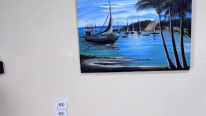 Una habitación con un cuadro colgado en la pared que muestra una escena costera, una bicicleta de mimbre y un enchufe.