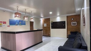 Una moderna zona de recepción con un mostrador central, un área de estar con sofás y una pared decorativa de madera.