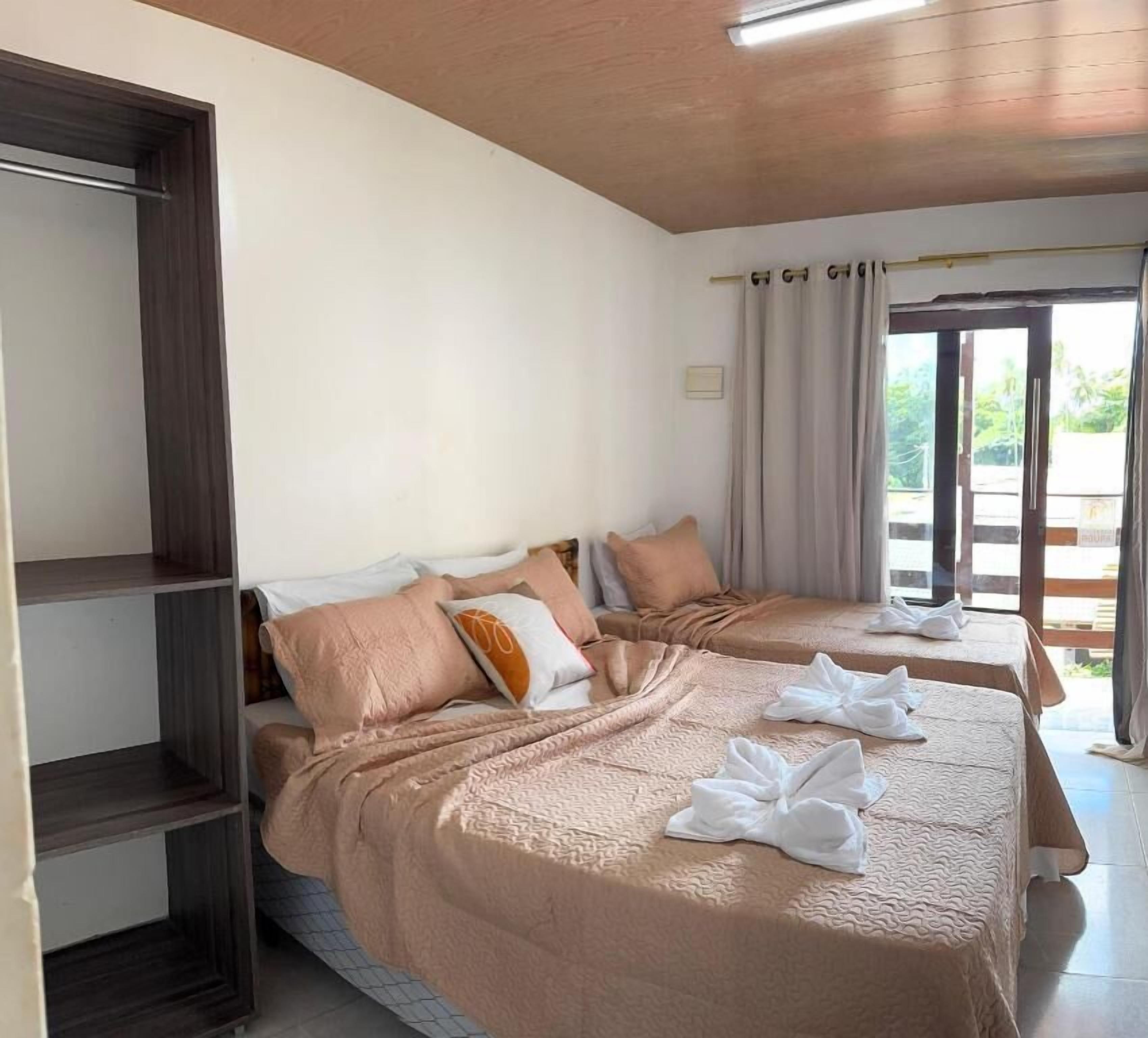 A hotel room with two beds, a wardrobe, and a view of the outdoors.