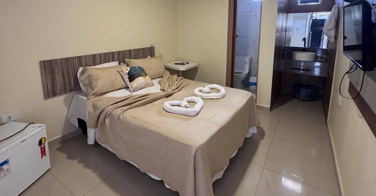 Habitación de hotel con cama, mesita de noche, pequeña mesa, baño y refrigerador.