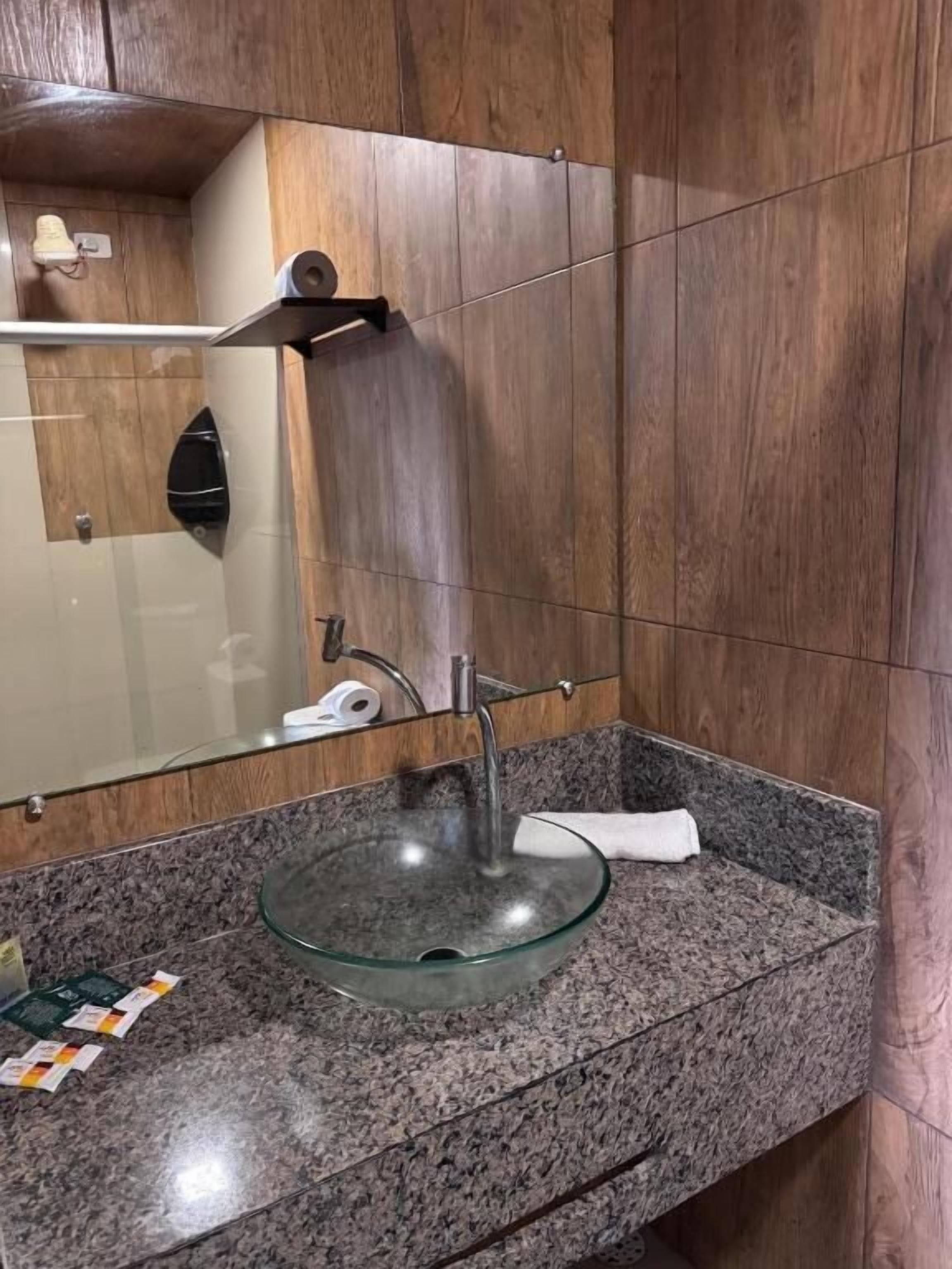 Un baño con un lavamanos de vidrio, paneles de madera y un espejo.