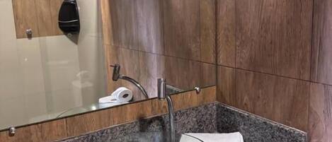Un baño con un lavamanos de vidrio, paneles de madera y un espejo.