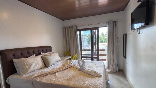 Habitación de hotel con cama, cortinas, televisor y vistas al exterior.