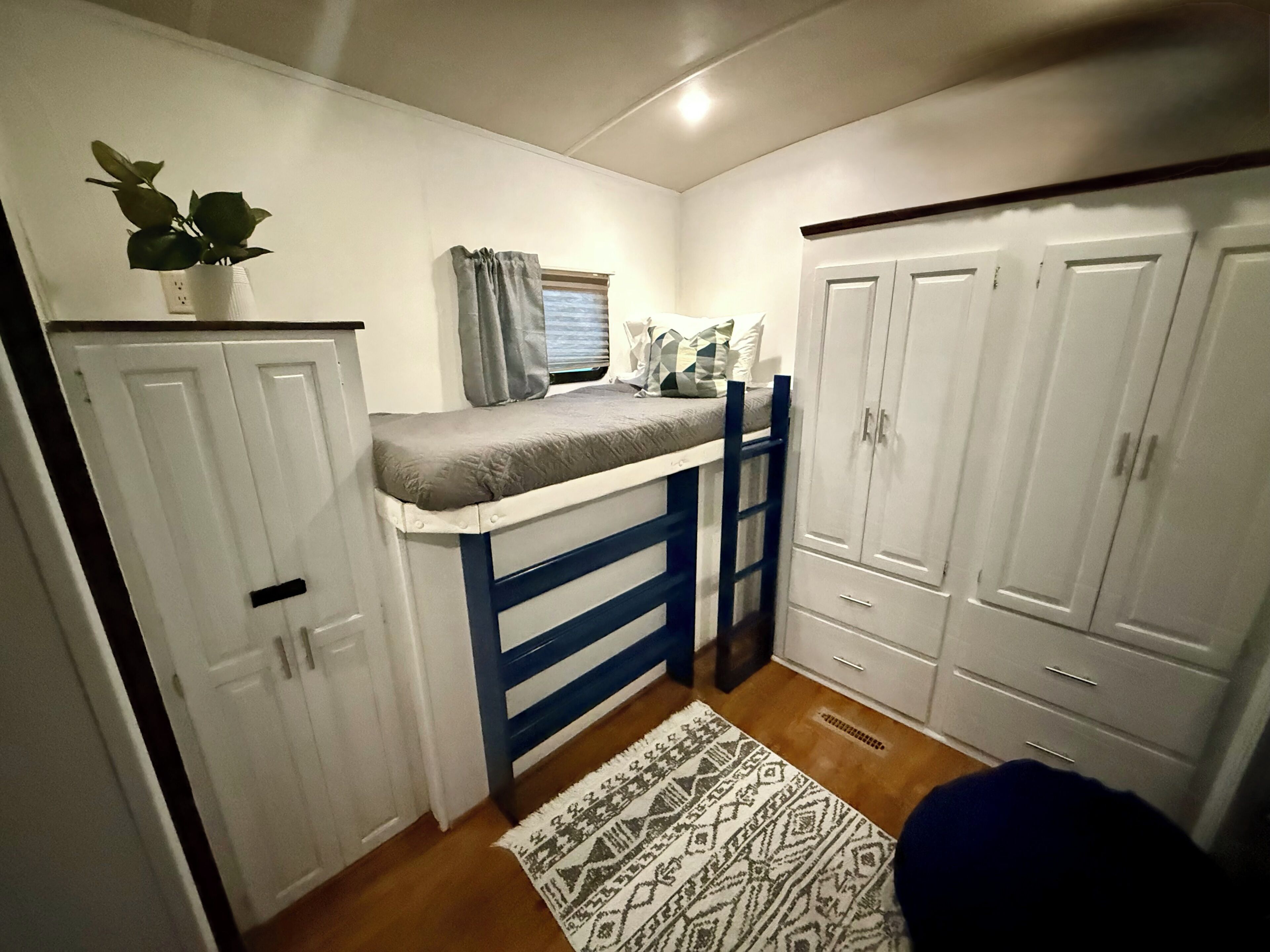 A compact bedroom with a bunk bed, a wardrobe, and a small window with curtains.