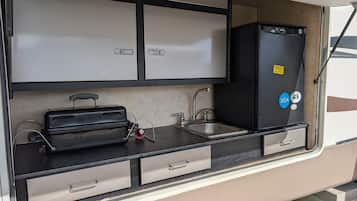 Una kitchenette compacta con un lavabo, estufa y armarios de almacenamiento.
