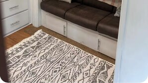 Un lit superposé avec une étagère inférieure, une armoire blanche et un tapis à motifs.